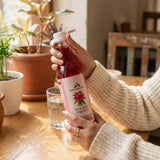 Person holding Buransh Squash bottle indoors ready to prepare a refreshing drink