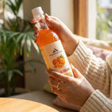 Person holding Mountain Haat Malta Squash bottle at home before serving