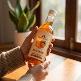 Mountain Haat Malta Squash 500ml classic version held in hand near window in natural light.